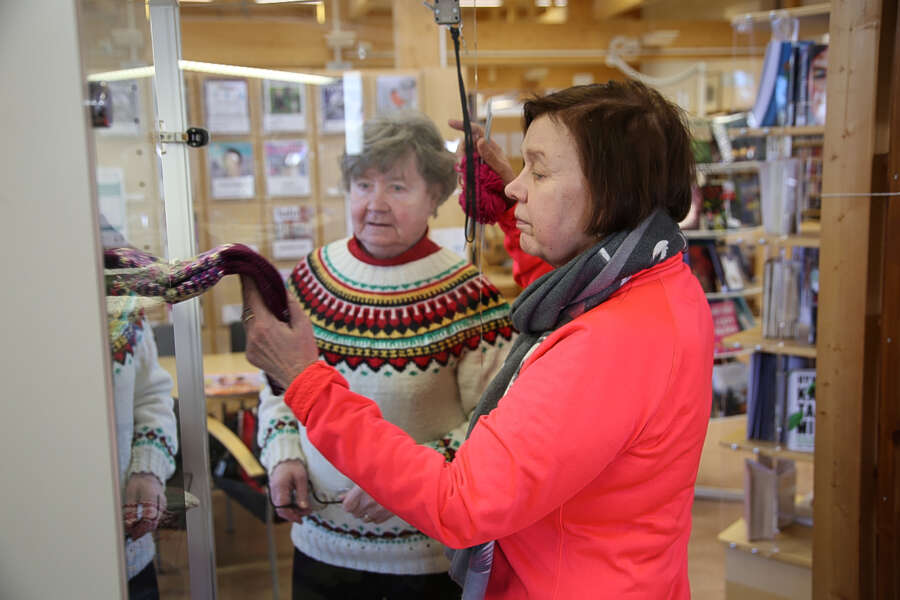 Leila Venäläinen seuraa vierestä, kun Pirjo-Liisa Valtanen etsii sukkia Riihikosken kirjastossa sijaitsevasta Kätevien käsien myyntivitriinistä.